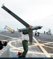 Матрос переносит БПЛА Boeing Insitu ScanEagle по взлетно-посадочной площадке десантного корабля Galicia ВМС Испании - на заднем плане слева видна катапульта для запуска, справа - устройство для посадки данного БПЛА.